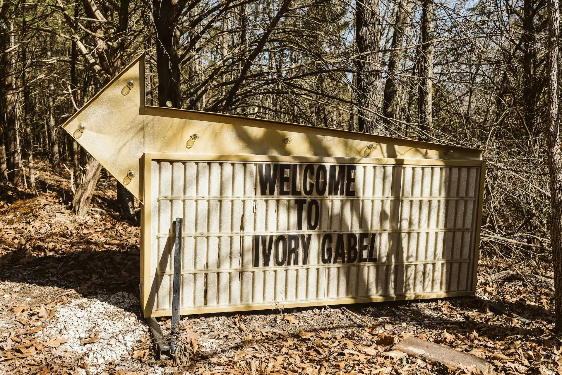 A hand-lettered “Welcome to Ivory Gabel” sign at the edge of the woods