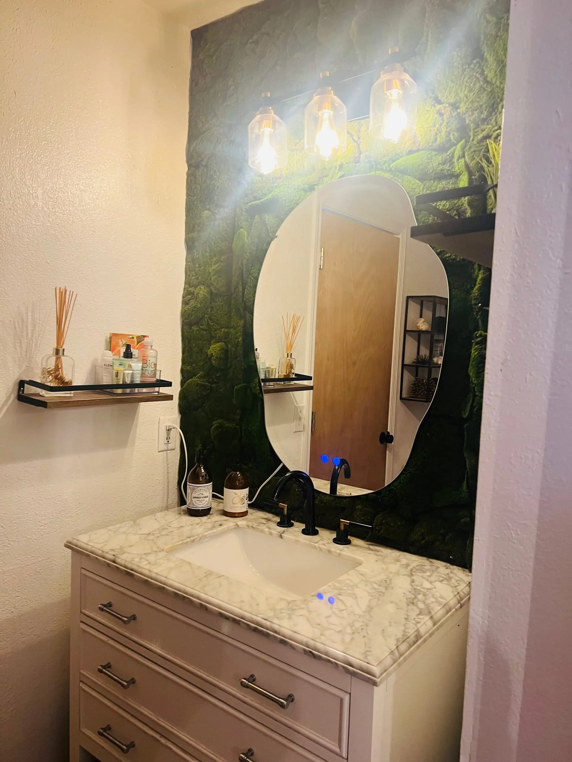 The bathroom vanity with an oval mirror, stone counter and a moss wall accent