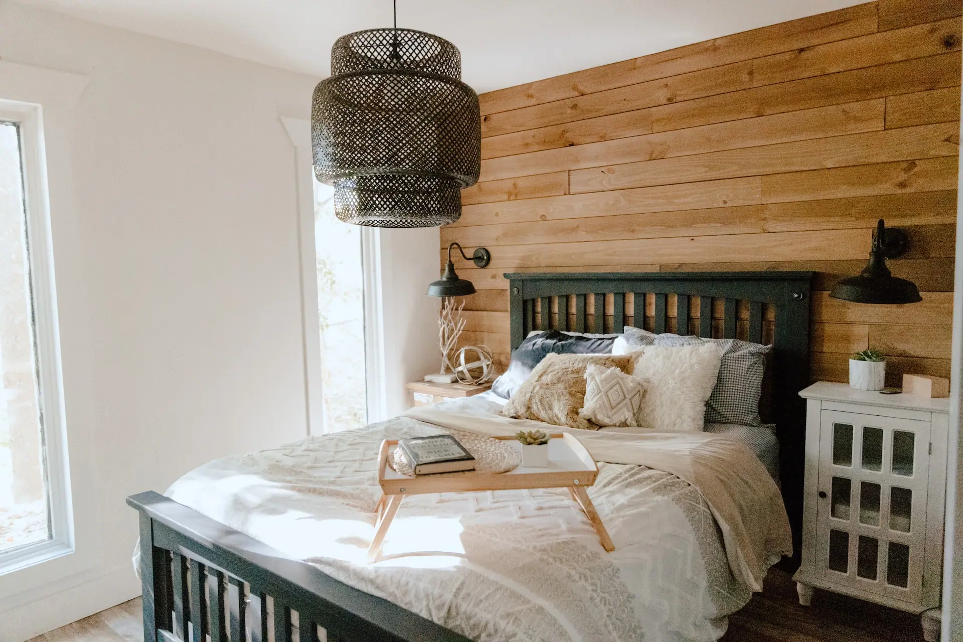 Bedroom 1 — a queen bed against a wood plank wall, with a woven pendant light and a breakfast tray