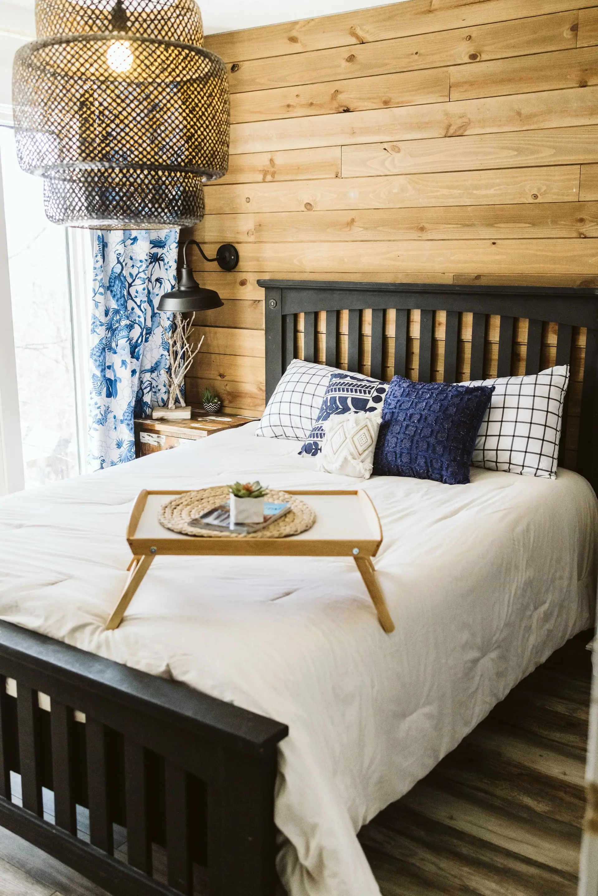 Bedroom 1 — a queen bed dressed in white linens with navy accents beside a patterned curtain