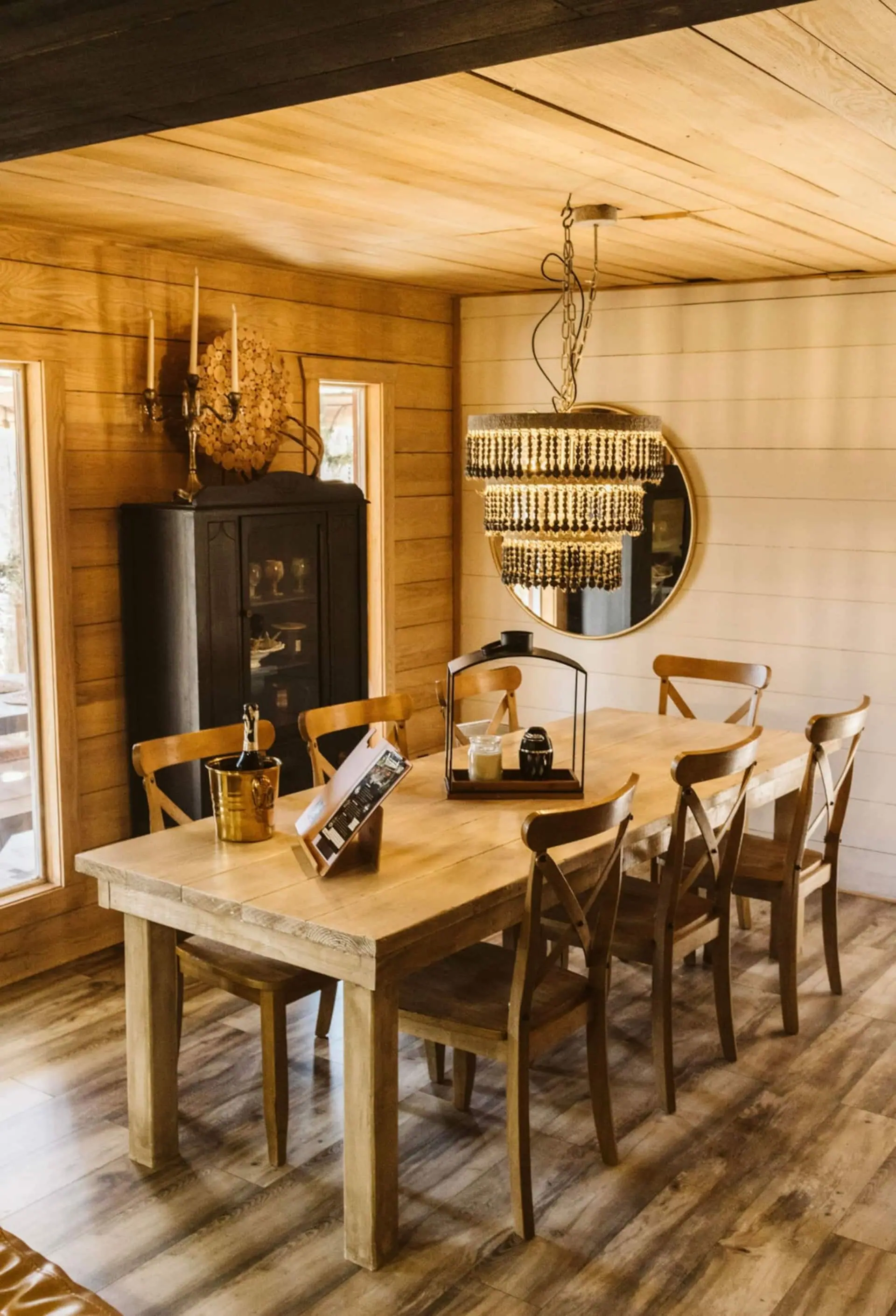 The dining table for six with a black hutch, round gold mirror and warm wood walls