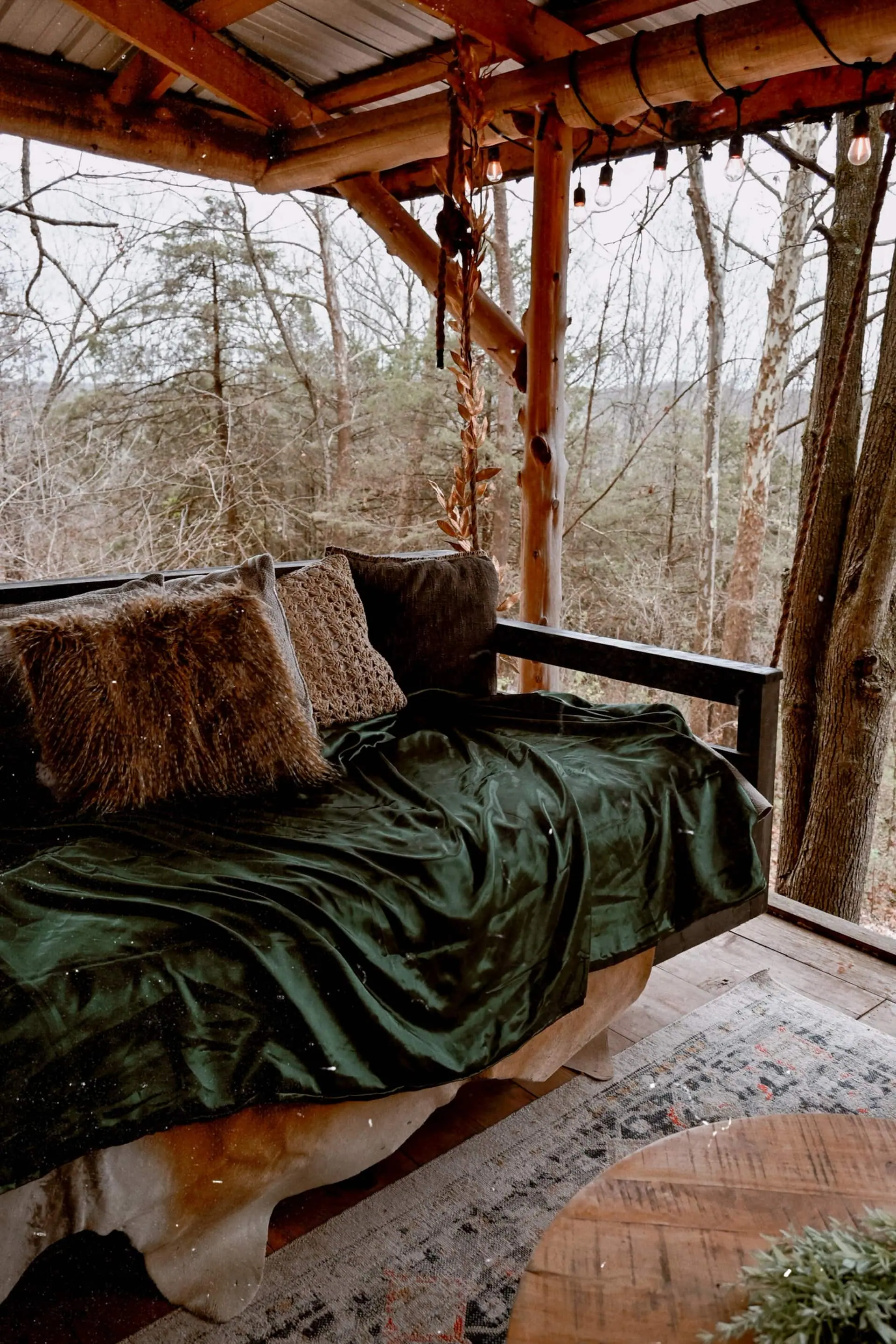 The porch swing bed piled with a moss-green blanket and sheepskin pillows