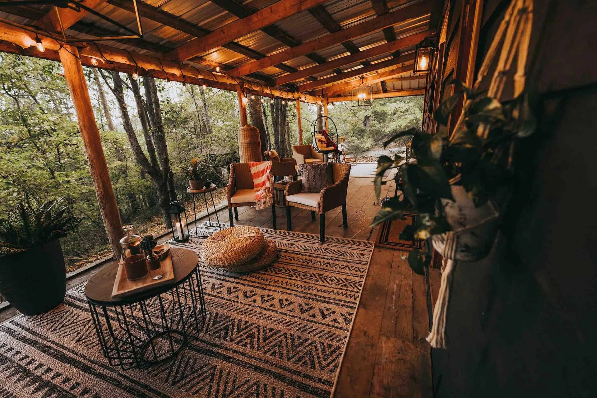 The panoramic wraparound porch with patterned rugs, woven chairs and a view straight into the trees
