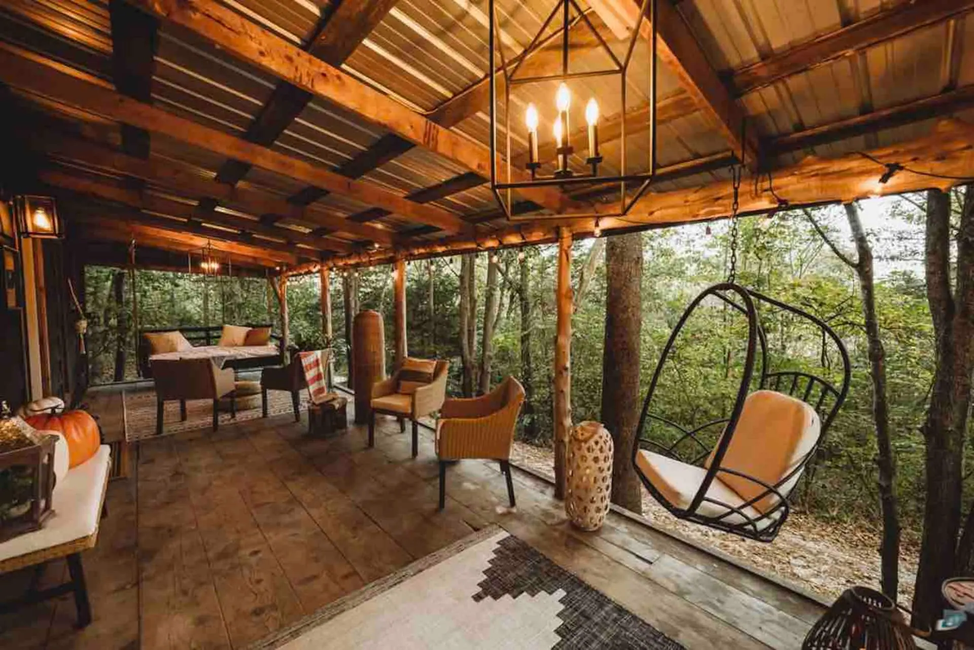 The wraparound porch with a hanging egg chair and outdoor dining under a timber roof